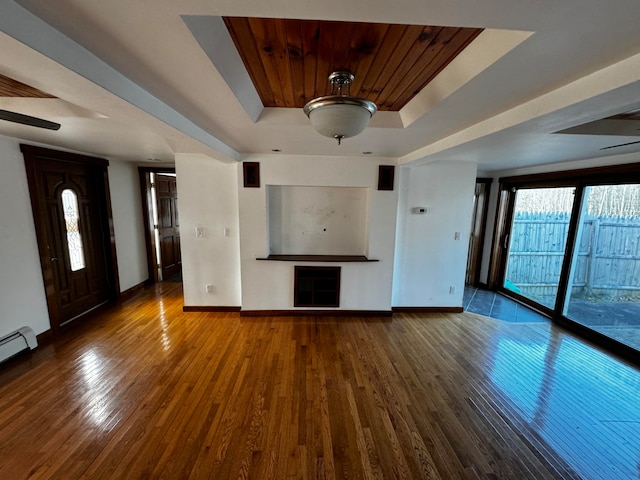 unfurnished living room with hardwood / wood-style floors, baseboard heating, a raised ceiling, and ceiling fan