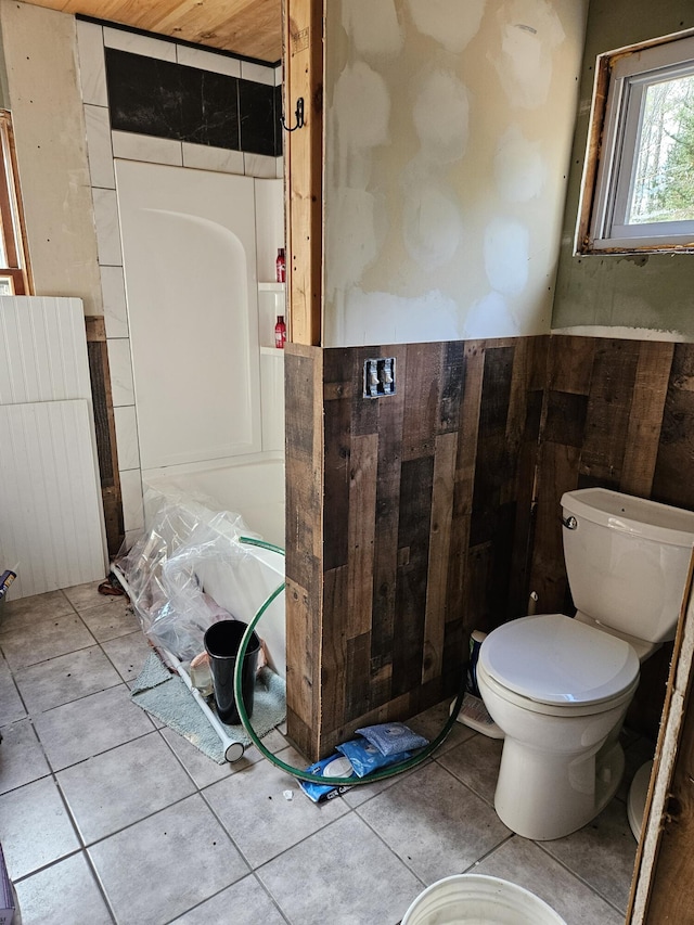 bathroom with tile patterned floors, toilet, and wooden walls