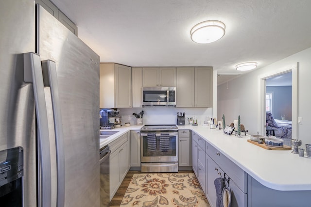 kitchen with kitchen peninsula, gray cabinets, light hardwood / wood-style floors, and appliances with stainless steel finishes