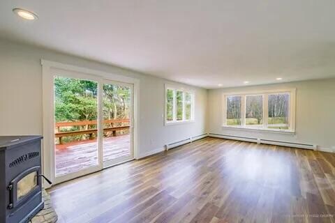 unfurnished living room with hardwood / wood-style flooring, a wood stove, and a baseboard radiator