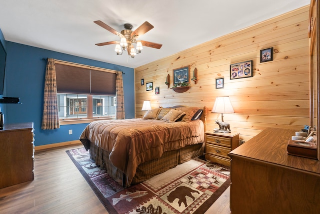 bedroom featuring hardwood / wood-style flooring, ceiling fan, and wooden walls