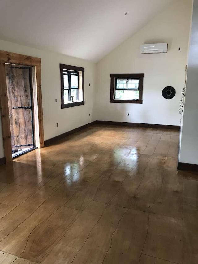 unfurnished room featuring an AC wall unit, baseboards, and high vaulted ceiling