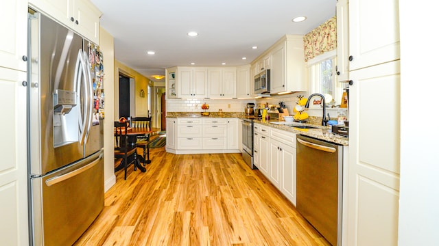 kitchen featuring light stone countertops, sink, light hardwood / wood-style floors, white cabinets, and appliances with stainless steel finishes