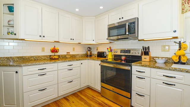 kitchen with dark stone counters, decorative backsplash, light wood-type flooring, appliances with stainless steel finishes, and white cabinetry