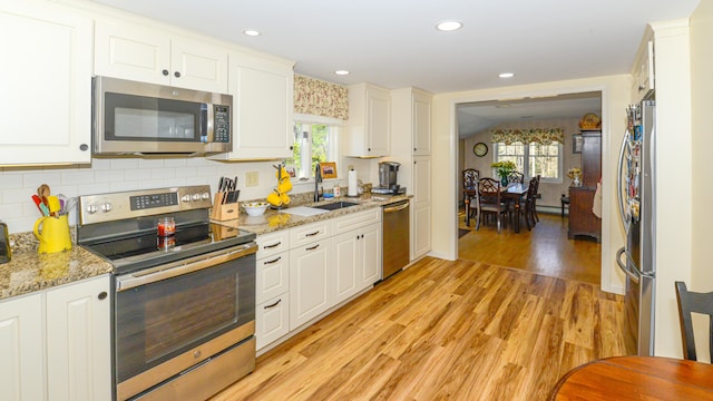 kitchen with a wealth of natural light, white cabinets, stainless steel appliances, and light hardwood / wood-style floors