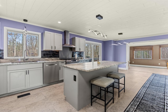 kitchen featuring a center island, wall chimney exhaust hood, sink, pendant lighting, and appliances with stainless steel finishes