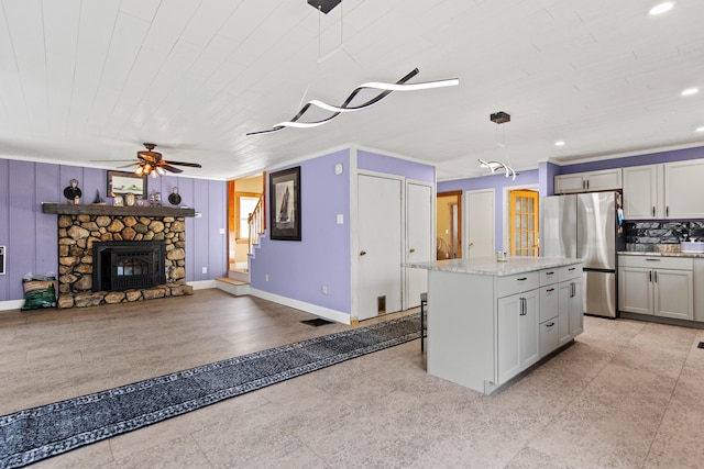 kitchen featuring a stone fireplace, a center island, decorative backsplash, stainless steel refrigerator, and decorative light fixtures