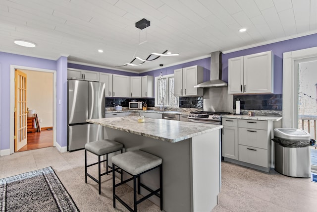 kitchen featuring stainless steel appliances, a center island, wall chimney range hood, a breakfast bar, and decorative light fixtures