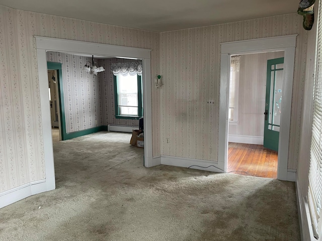 carpeted spare room featuring a baseboard radiator and a notable chandelier