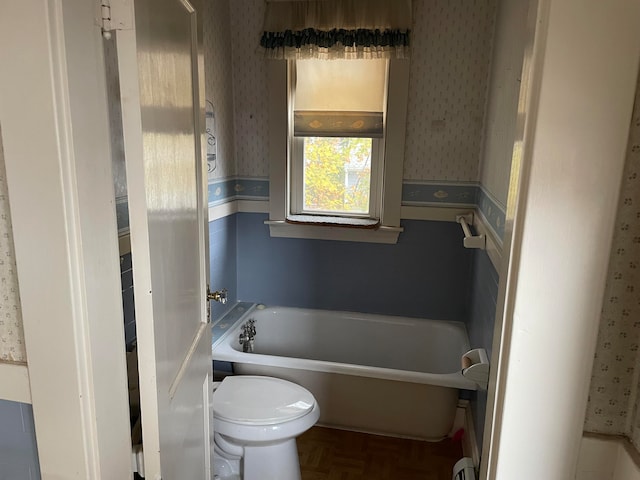 bathroom featuring a bathing tub, parquet floors, and toilet