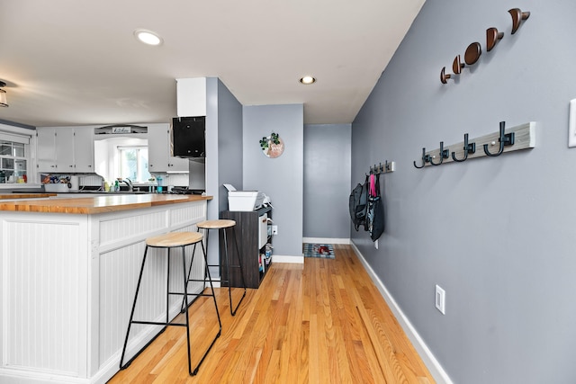 kitchen featuring butcher block counters, white cabinetry, sink, and light hardwood / wood-style floors