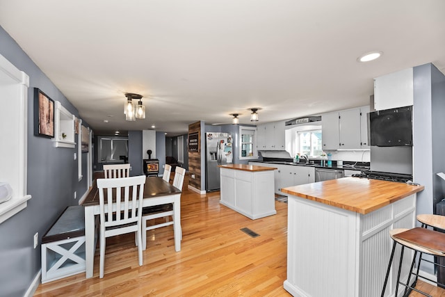 kitchen featuring stainless steel appliances, light hardwood / wood-style floors, a center island, white cabinets, and wood counters