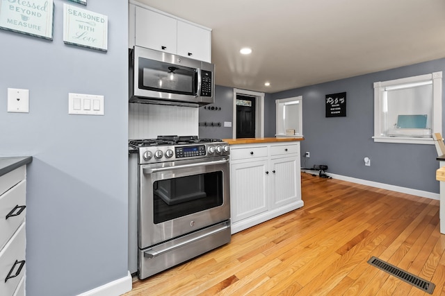 kitchen with stainless steel appliances, white cabinetry, and light hardwood / wood-style flooring