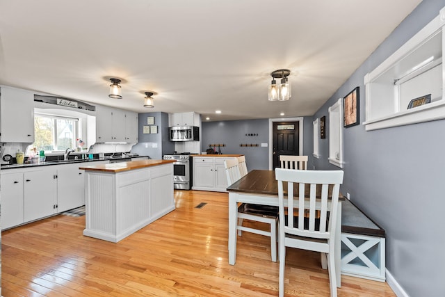 kitchen with white cabinets, light hardwood / wood-style flooring, appliances with stainless steel finishes, and a center island