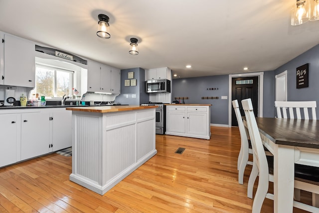 kitchen featuring white cabinetry, sink, appliances with stainless steel finishes, a kitchen island, and light wood-type flooring