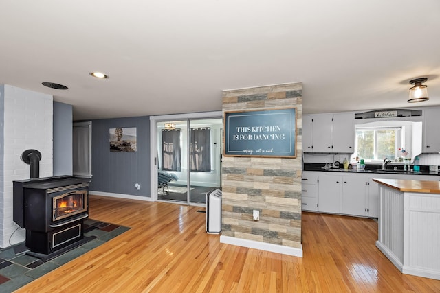 kitchen featuring white cabinets, light hardwood / wood-style floors, sink, and a wood stove