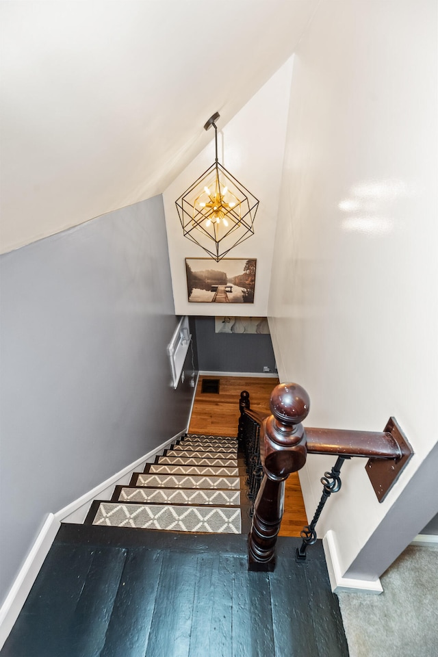 stairs with hardwood / wood-style floors, lofted ceiling, and a chandelier