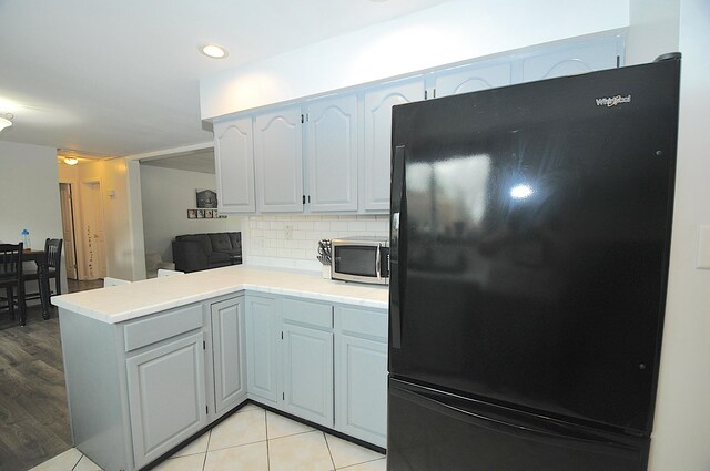 kitchen featuring kitchen peninsula, black fridge, decorative backsplash, and light wood-type flooring