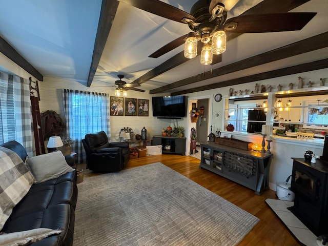 living room featuring a wood stove, hardwood / wood-style floors, beamed ceiling, and ceiling fan