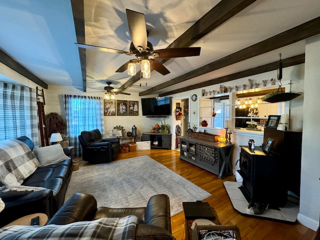 living room featuring ceiling fan, hardwood / wood-style flooring, beamed ceiling, and a wood stove