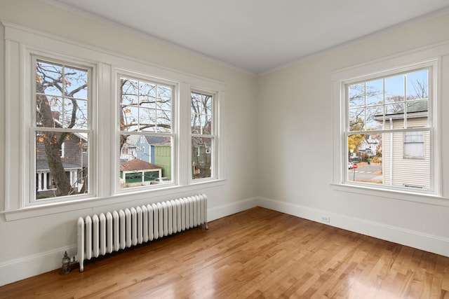 empty room featuring ornamental molding, light hardwood / wood-style floors, radiator heating unit, and a healthy amount of sunlight