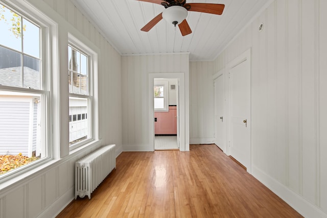 empty room with radiator heating unit, light hardwood / wood-style floors, ceiling fan, and plenty of natural light