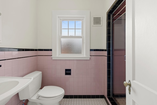 bathroom with tile walls, tile patterned flooring, walk in shower, and toilet