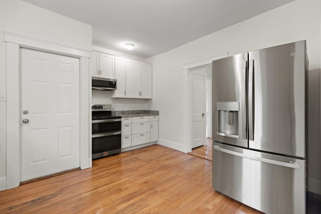 kitchen with stainless steel appliances, stone countertops, white cabinetry, and light hardwood / wood-style flooring