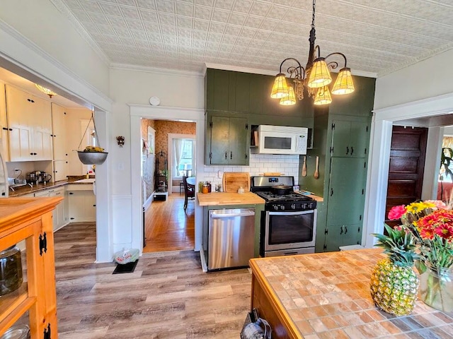 kitchen with appliances with stainless steel finishes, ornamental molding, light hardwood / wood-style flooring, pendant lighting, and decorative backsplash