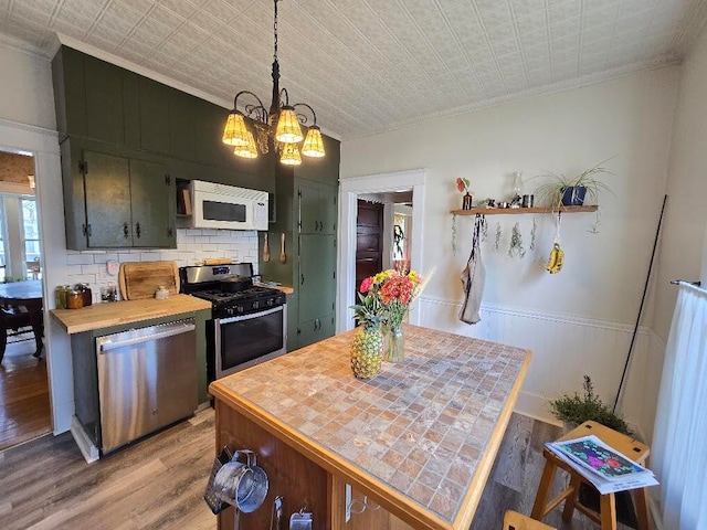 kitchen featuring light hardwood / wood-style floors, appliances with stainless steel finishes, backsplash, hanging light fixtures, and crown molding