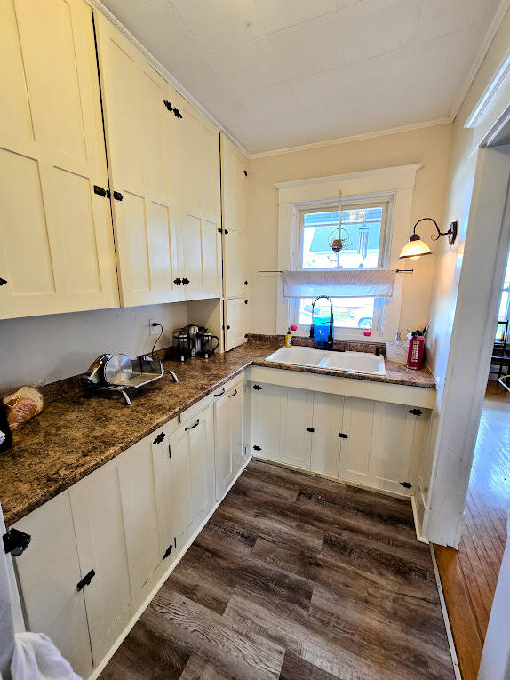 kitchen featuring white cabinetry, sink, ornamental molding, dark stone counters, and dark hardwood / wood-style flooring