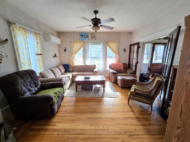 living room with a wall unit AC, light hardwood / wood-style floors, and ceiling fan