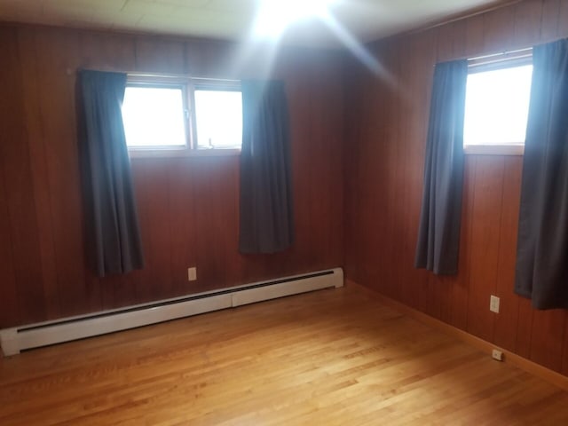 spare room featuring a baseboard heating unit, light hardwood / wood-style flooring, a healthy amount of sunlight, and wood walls