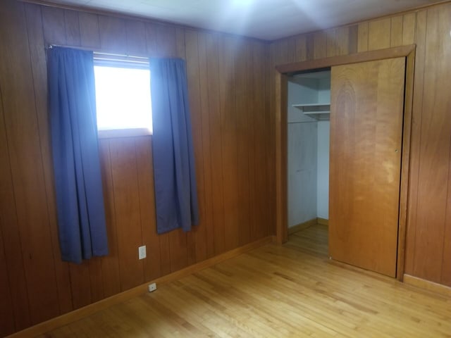 unfurnished bedroom with light hardwood / wood-style flooring, a closet, and wooden walls