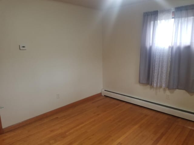 unfurnished room featuring hardwood / wood-style flooring and baseboard heating