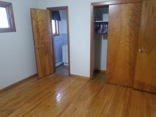 unfurnished bedroom featuring ensuite bathroom, light hardwood / wood-style floors, a closet, and a baseboard heating unit