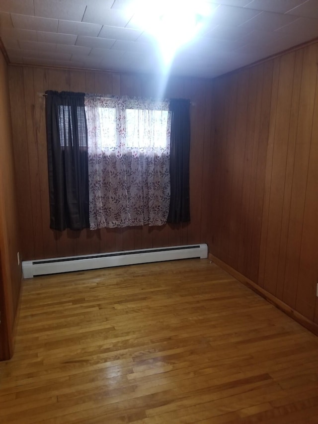 spare room with hardwood / wood-style floors, a baseboard heating unit, and wooden walls