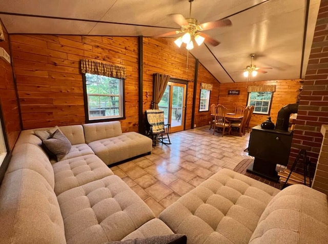 living room with a wood stove, lofted ceiling, ceiling fan, and wood walls