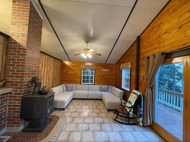 unfurnished living room featuring a wood stove, wood walls, ceiling fan, and vaulted ceiling