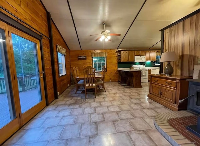 dining space featuring wood walls, a wealth of natural light, vaulted ceiling, and ceiling fan