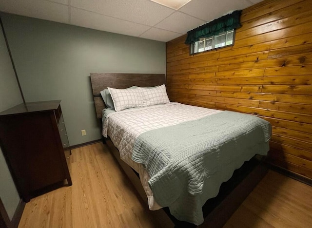 bedroom with wood walls, a drop ceiling, and light hardwood / wood-style floors