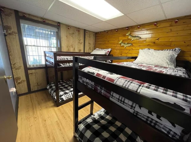 bedroom featuring a paneled ceiling, wooden walls, and light wood-type flooring