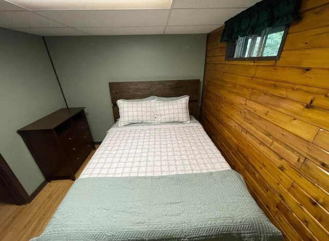 bedroom with a paneled ceiling, hardwood / wood-style flooring, and wooden walls