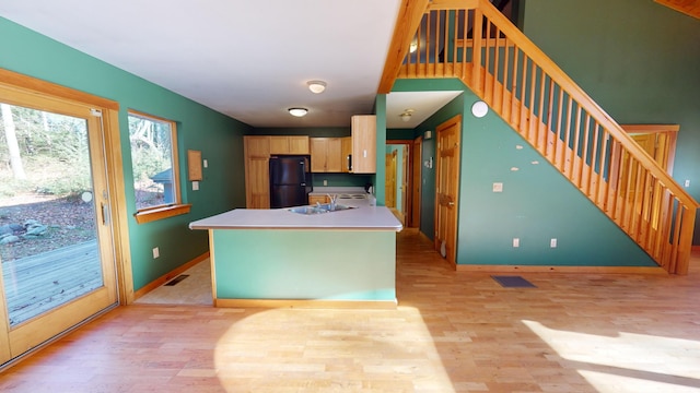 kitchen with black fridge, sink, light brown cabinetry, a kitchen island with sink, and light wood-type flooring