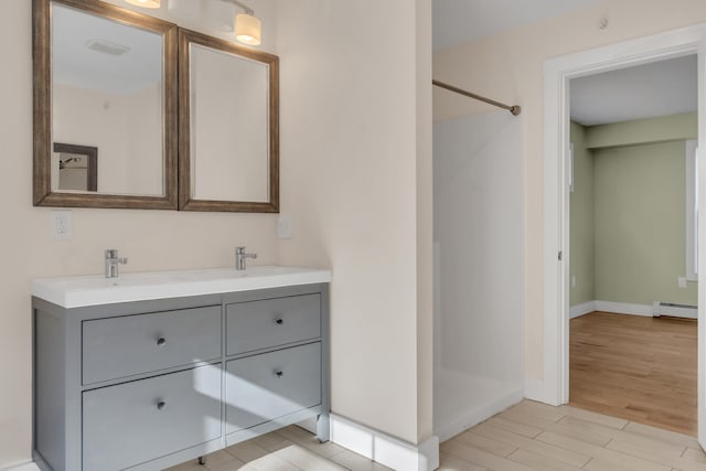 bathroom with hardwood / wood-style floors, walk in shower, vanity, and a baseboard heating unit