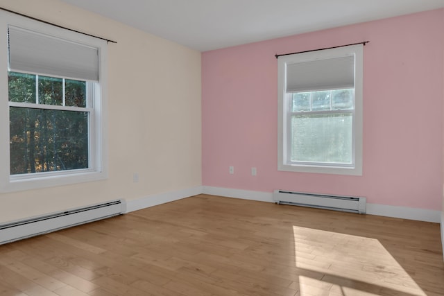 empty room featuring a wealth of natural light, light hardwood / wood-style flooring, and a baseboard heating unit