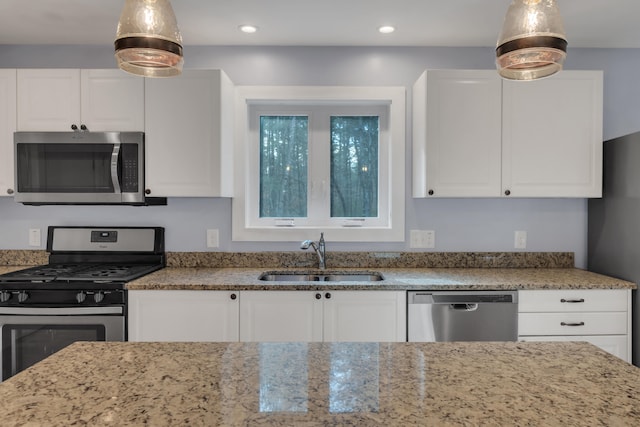 kitchen with stainless steel appliances, pendant lighting, sink, light stone countertops, and white cabinetry