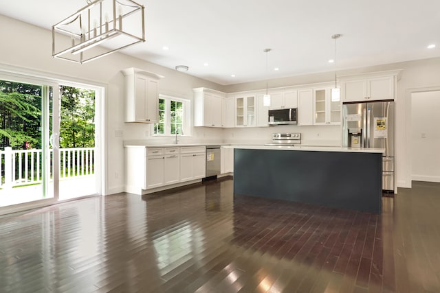 kitchen with stainless steel appliances, a kitchen island, white cabinetry, decorative light fixtures, and dark wood-type flooring