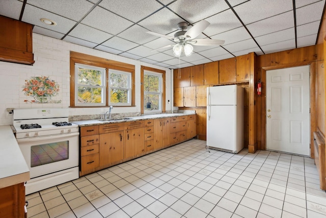 kitchen featuring a drop ceiling, wooden walls, sink, ceiling fan, and white appliances