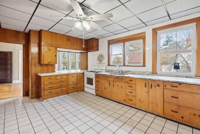 kitchen featuring white range with gas cooktop, wooden walls, sink, and a drop ceiling